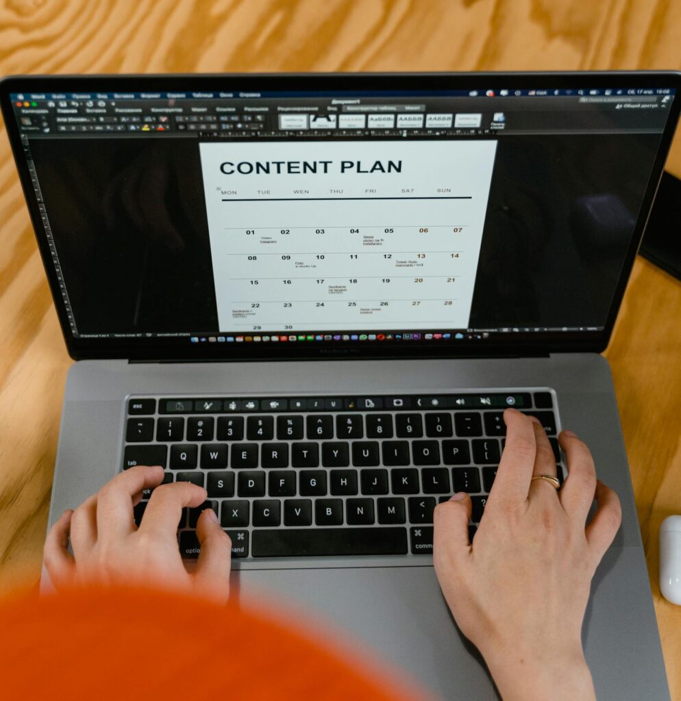 Hands typing on a laptop keyboard displaying a content plan on screen.