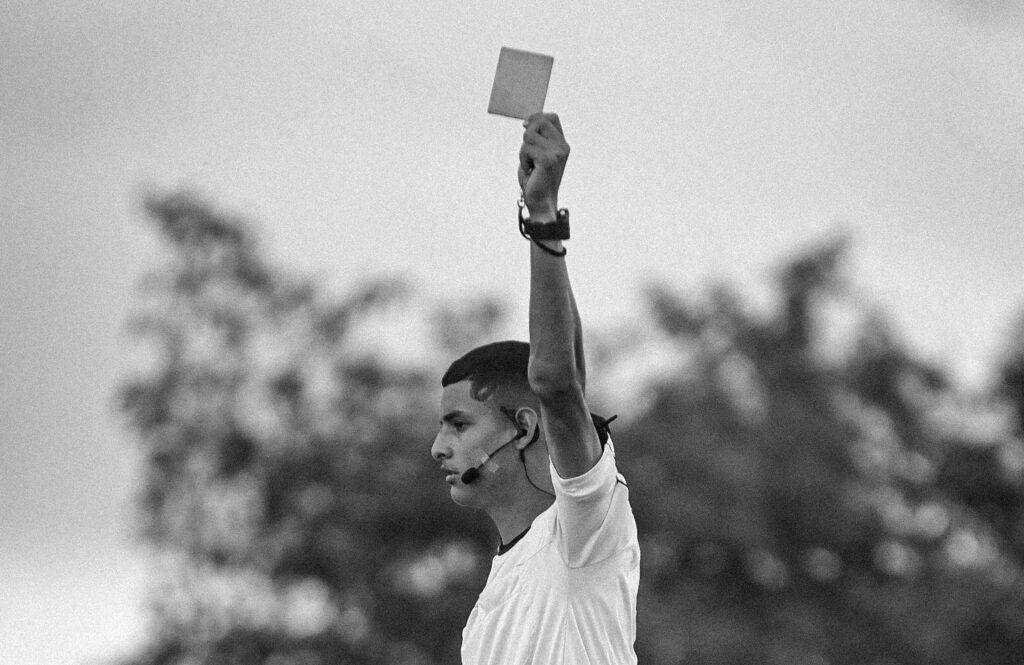 Black and white image of a referee showing a yellow card during a soccer match.